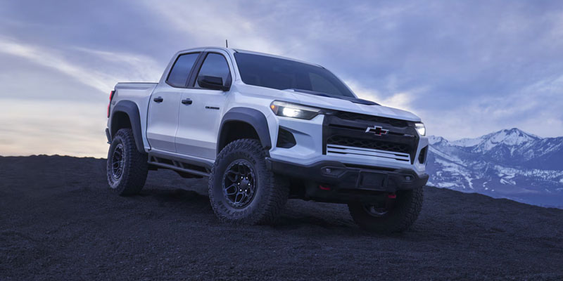 White Chevrolet Colorado ZR2 pickup truck parked on rugged terrain with snowy mountains in the background